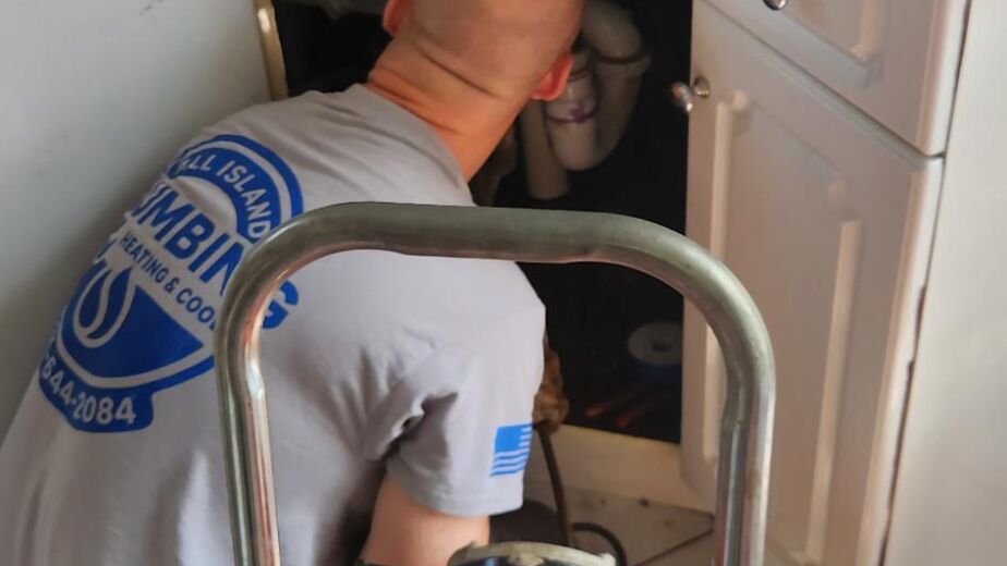 Plumber from All Island Plumbing inspecting kitchen sink drain for clogs, emphasizing professional drain cleaning services and maintenance.