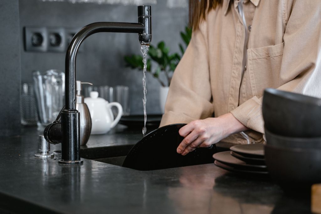 Woman in beige shirt washing dishes in a functional sink after repair.